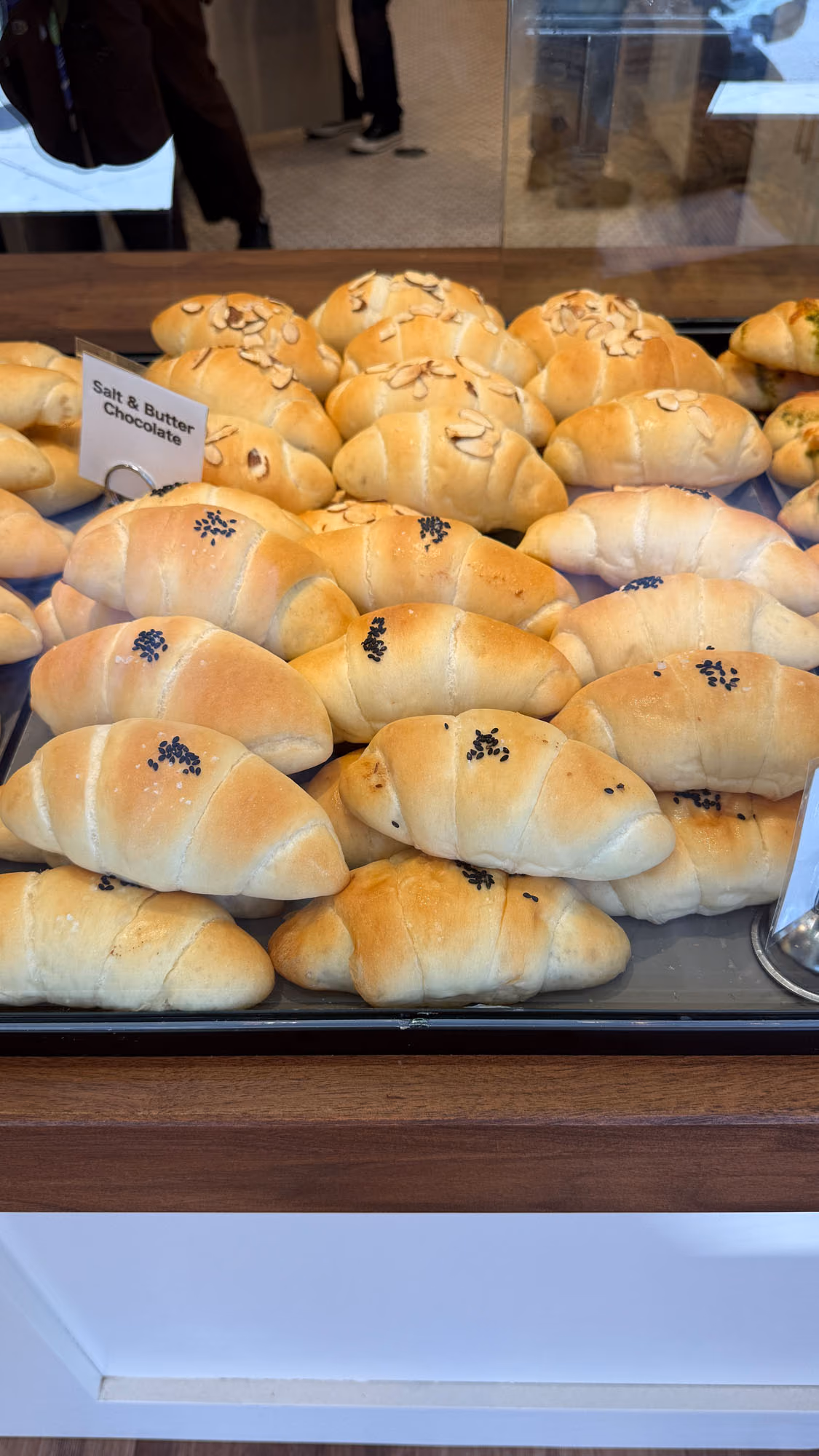 A bakery case filled with croissant rolls topped with sliced almonds and black sesame seeds.